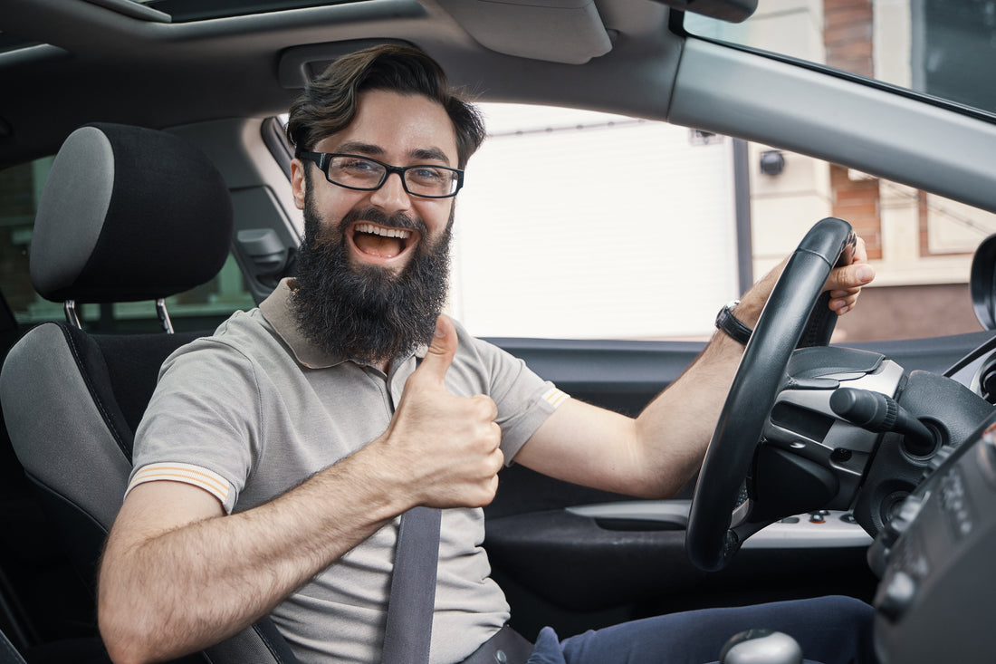 Man smiling in driver’s seat giving a thumbs up inside a car, suggesting improved comfort and quieter cabin after car audio sound deadening installation